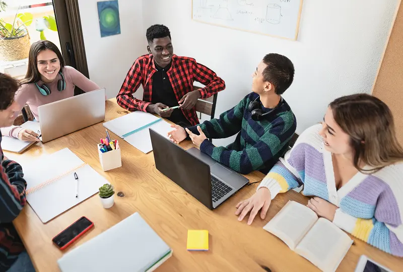 Students collaborating around a table with laptops.