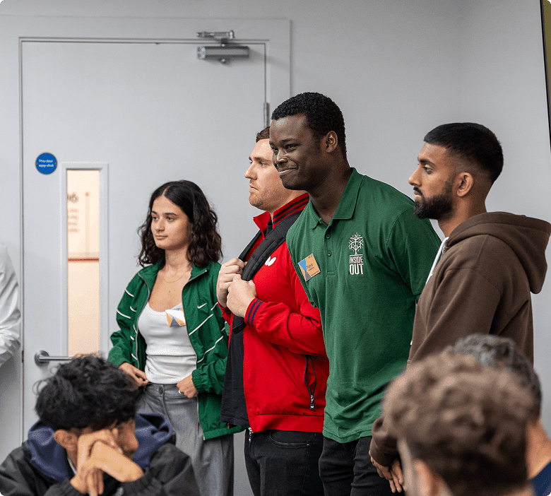 Four people standing, engaging with seated audience.